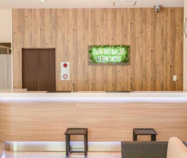 Wooden reception desk with green LiVEMAX sign and stools at LiVEMAX RESORT Kusatsu Onsen, Gunma, Kanto