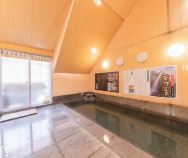 Indoor communal onsen bath with stone tiles and wooden vaulted ceiling at LiVEMAX RESORT Kusatsu Onsen in Gunma