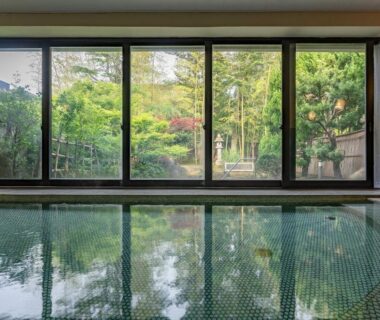 Indoor tiled onsen bath with large windows overlooking garden lantern at Livemax Resort Yuhigaura, Kyoto