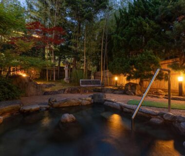 Outdoor stone onsen bath with rock edging and lantern lighting at Livemax Resort Yuhigaura Kyoto