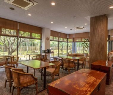 Sunlit lounge with wooden tables and garden views at Livemax Resort Yuhigaura Kitu Onsen, Kyoto Kansai