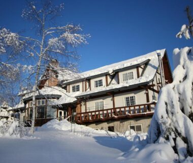 Chalet-style lodge blanketed in deep snow with fir trees and blue sky at Lodge Clubman, Iwate