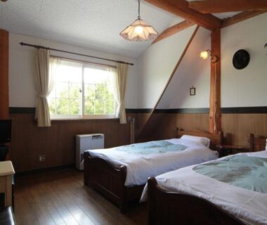 Twin wooden beds, exposed ceiling beams, hardwood floor and window in Lodge Clubman room, Iwate