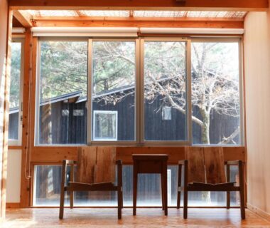 Interior wooden lounge with two chairs and small table facing large windows overlooking trees at Lodge Toranoyu Ōita