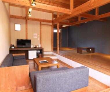 Spacious wooden interior with raised platform, low table, sofas and exposed ceiling beams at Lodge Toranoyu in Ōita