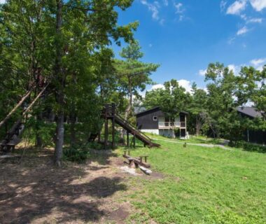 Children's playground and grassy courtyard beside Lodge Toranoyu buildings under blue sky in Ōita, Kyūshū, Japan