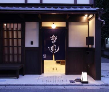 Traditional wooden entrance with noren curtain and warm lantern light at Luck You Kyoto in Kansai
