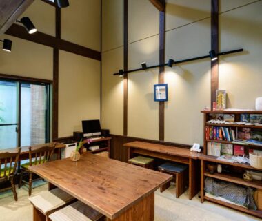 Communal wooden dining table and benches with bookshelf and garden view at Luck You Kyoto, Kyoto, Kansai, Japan