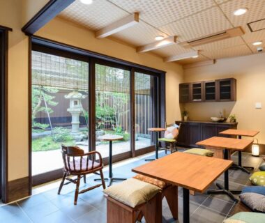 Interior lounge with wooden tables, floor cushions, sliding glass to courtyard garden at Luck You Kyoto Kyoto