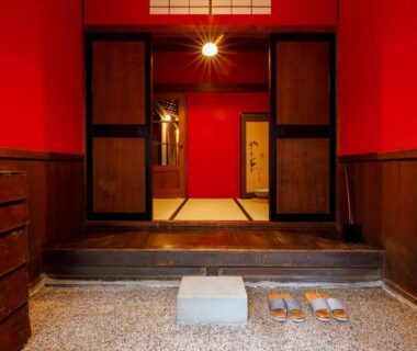 Red-walled genkan with stone step, wooden sliding doors and slippers at Machi no Odoriba Ishikawa Chūbu