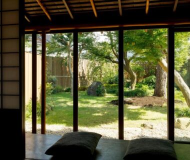 Traditional tatami room with low cushions and sliding doors opening to a quiet garden at Machi no Odoriba in Ishikawa