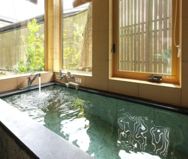 Stone indoor bath with wooden blinds and small garden view at Machi no Odoriba, Ishikawa