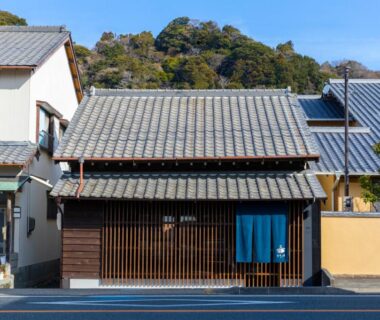 Traditional wooden facade with blue noren at Machihaku 456 in Shizuoka, tiled roof and hillside backdrop