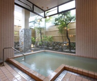 Tiled indoor onsen bath with glass wall overlooking small rock garden at Manseiro in Wakayama