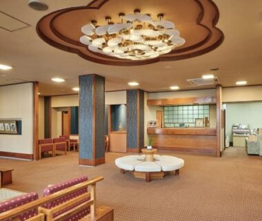Warm ryokan lobby with reception desk, seating area, chandelier and brochure racks at Manseiro in Wakayama, Kansai