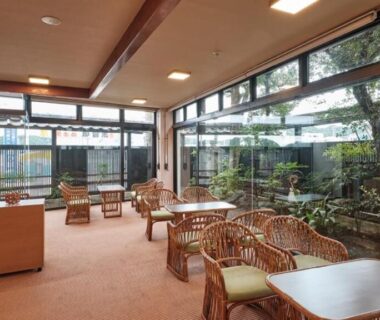 Ryokan lounge with rattan chairs and floor-to-ceiling windows overlooking courtyard garden at Manseiro in Wakayama