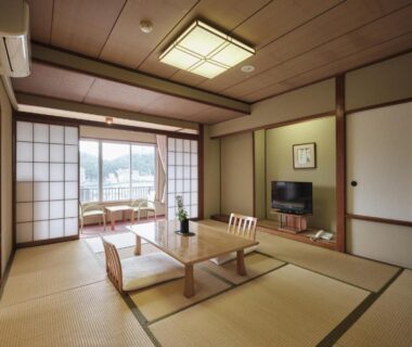 Spacious tatami room with low table, shoji screens and balcony overlooking wooded hills at Manseiro in Wakayama
