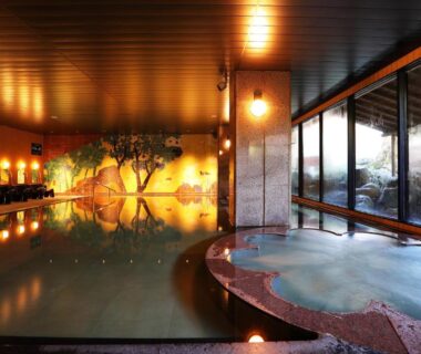 Spacious indoor onsen with stone edge, wooden ceiling and glass wall at Manten no Tsujinoya, Ishikawa