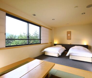Tatami seating and low table with two beds and large window overlooking trees at Manza Onsen Nisshinkan, Gunma