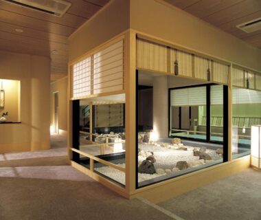 Glass-enclosed indoor rock garden with white pebbles, stone accents, wooden frames and shoji screens inside Maruei ryokan