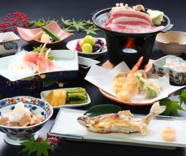 Assorted traditional Japanese dishes on lacquer trays with grilled fish, tempura, sashimi and small bowls at Maruka Ryokan Nagano