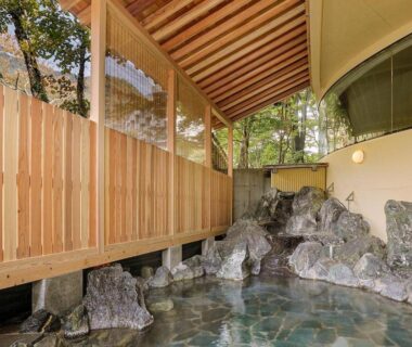 Covered rock-lined onsen bath with wooden privacy fence and natural stone edging at Marumine Kanko Hotel, Fukushima