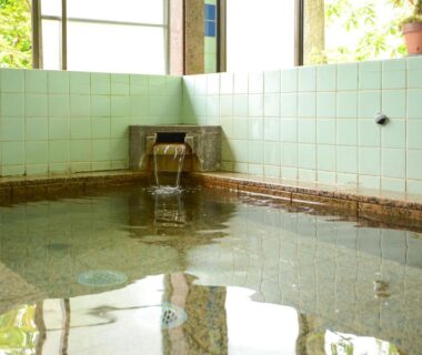 Indoor tiled onsen bath with water spout and window light at Maruyaso in Yamanashi