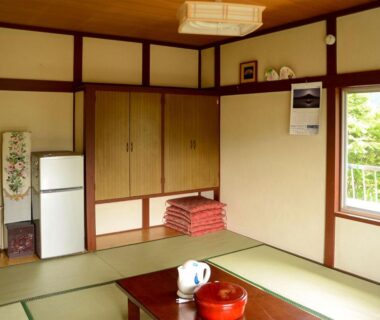 Traditional tatami room with low table, stacked futon and window overlooking greenery at Maruyaso, Yamanashi