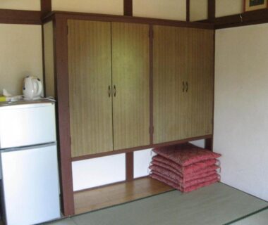 Tatami room with wooden cabinets, stacked cushions, kettle and fridge at Maruyaso, Yamanashi, Chūbu