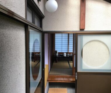 Narrow tatami corridor leading to a room with shoji screens and circular sliding panel at Masugataya Ryokan, Chiba