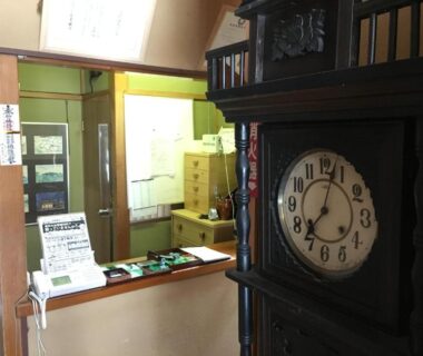 Wooden antique clock foreground with reception counter, key boxes and paperwork at Masugataya Ryokan in Chiba