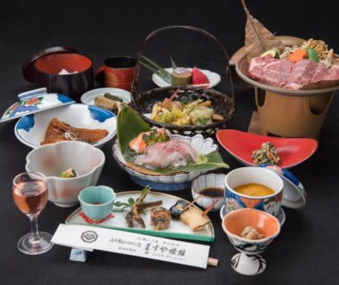 Multi-dish Japanese dinner with sashimi, soup bowls, and small pot at Masuya Ryokan Nagano