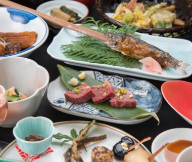 Plated assortment of Japanese dishes with grilled fish, sliced meat, skewers and small side bowls