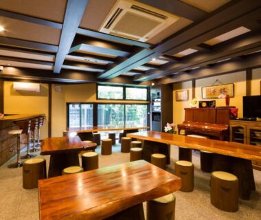 Lounge with wooden tables, round stools, exposed beams, bar counter and large windows at Matsubaya Ryokan, Kyoto