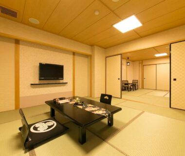 Spacious tatami room with low dining table, floor cushions, sliding fusuma doors and wall-mounted television at Matsui-Bekkan Hanakanzashi Kyoto