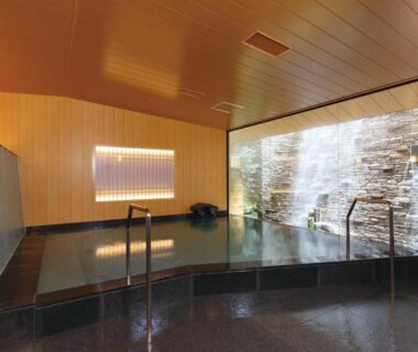 Indoor soaking bath with stone waterfall wall and wooden ceiling at Matsui Honkan in Kyoto Kansai