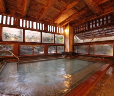 Indoor communal onsen with wooden beams and large windows at Matsukaneya Annex, Yamagata