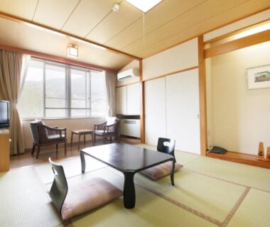 Traditional tatami room with low table, zabuton cushions, tokonoma alcove and window seating at Matsukaneya Annex, Yamagata