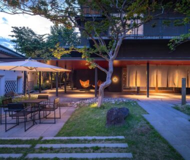 Evening courtyard with outdoor seating, umbrellas, stone path and illuminated ryokan entrance in Nagano