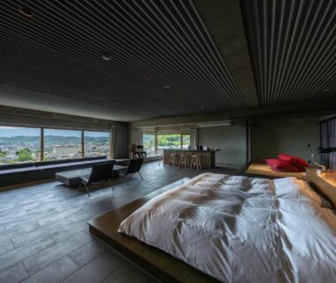 Spacious room with low futon on wooden platform and panoramic windows framing Nagano mountain views