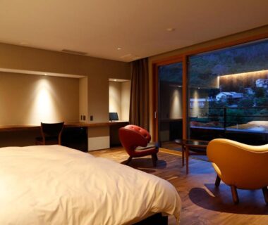 Bedroom with bed, lounge chairs and floor-to-ceiling window overlooking garden at Matsumoto Jujo, Nagano