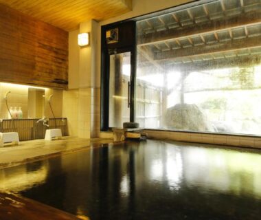 Interior onsen bath with wooden edge, washing stations and large garden-facing window at Matsunoi, Gifu