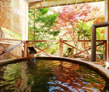 Round wooden outdoor onsen with autumn maple foliage at Matsunoi, Gifu