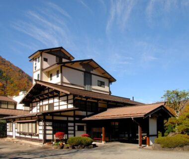 Exterior view of a traditional multi-story ryokan with wooden beams and mountain backdrop in Gifu