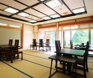 Spacious tatami dining area with low tables and wooden chairs overlooking garden greenery through large windows