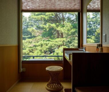 Tatami room with low stool, wooden sink and large window overlooking lush pine trees
