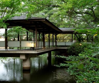 Covered wooden corridor over reflective pond in lush ryokan garden at Matsusaki, Ishikawa, Japan