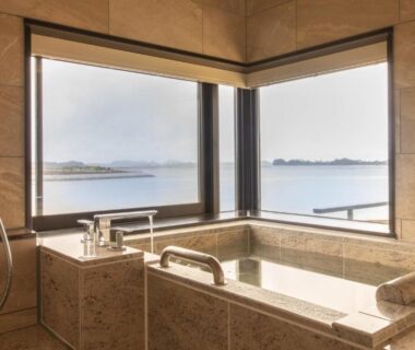 Stone soaking tub beside corner windows with coastal island views at Matsushima Ichinobo, Miyagi Tōhoku