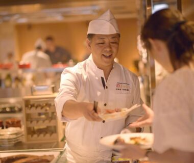 Smiling chef in uniform handing a plate to a guest at Matsushima Ichinobo dining area in Miyagi