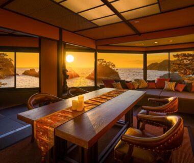 Tatami room with low table, cushioned seating and large windows framing a golden coastal sunset view
